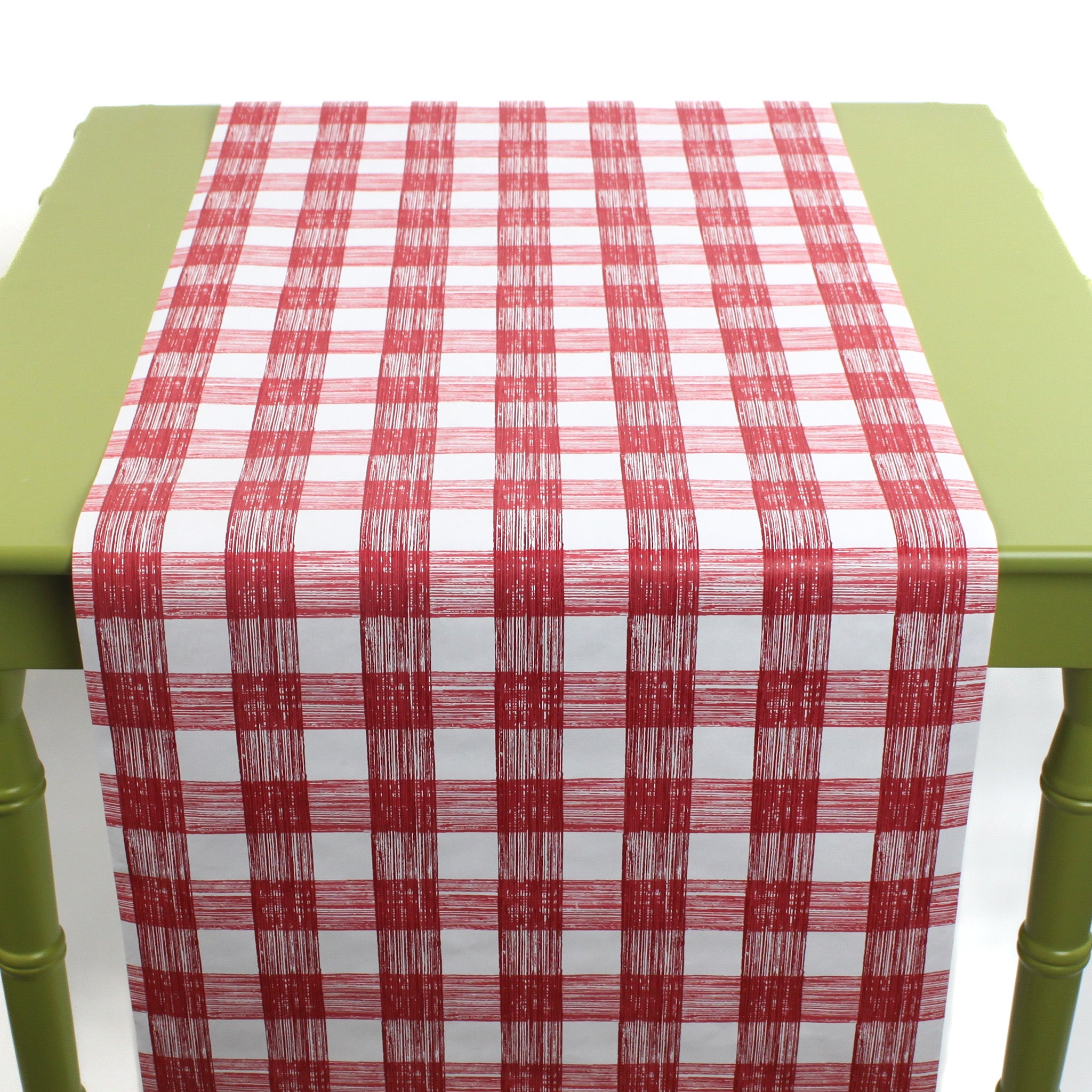 a green table covered by a Gin Lane Red Gingham Paper Table Runner on a white background