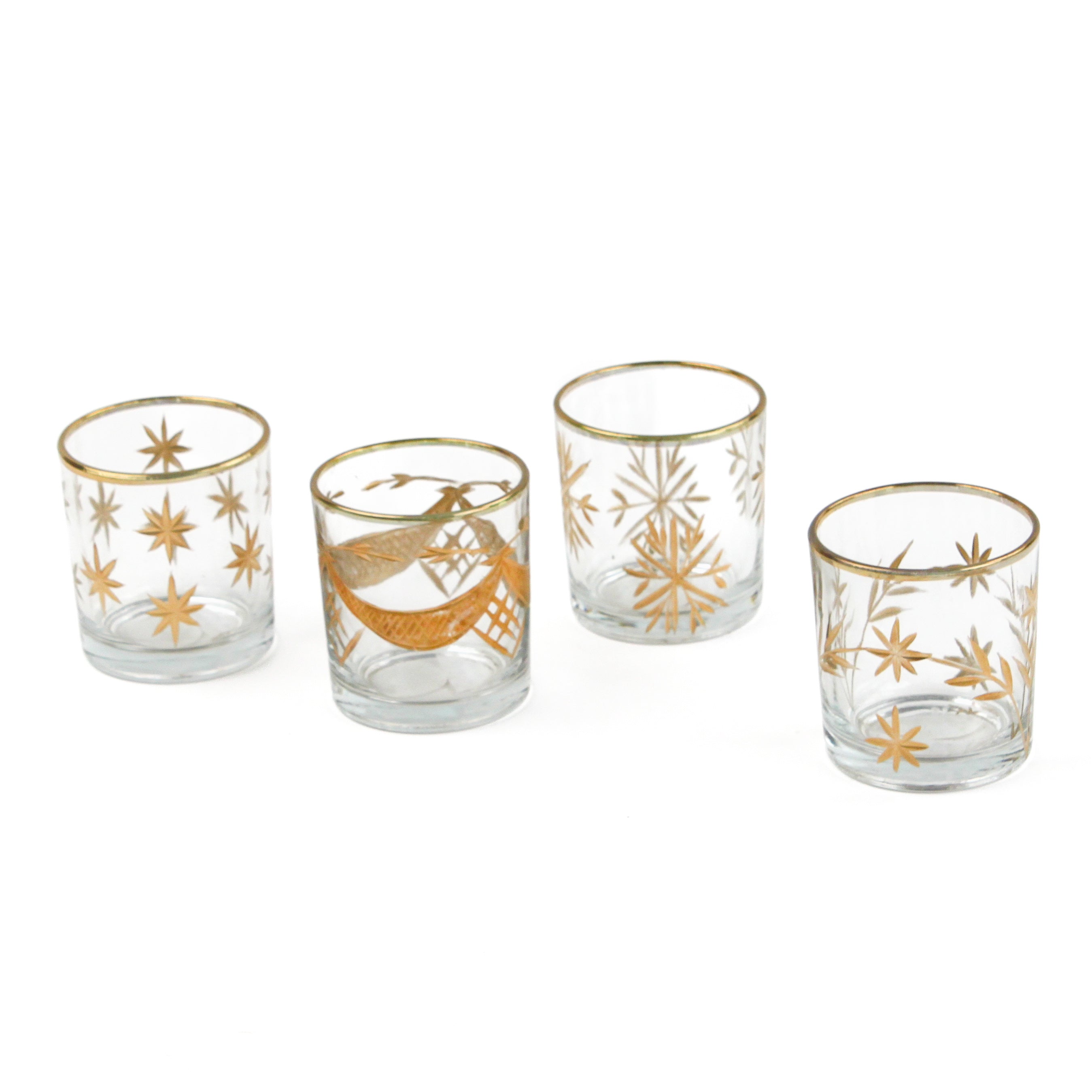 Set of four clear glass candle holders with gold decorative patterns on a white background