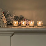Decorative candles in glass holders on a mantelpiece with Christmas decorations.