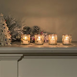 Decorative candles in glass holders on a mantelpiece with Christmas decorations.