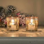 Two lit candles in decorative glass holders with floral arrangements in the background.