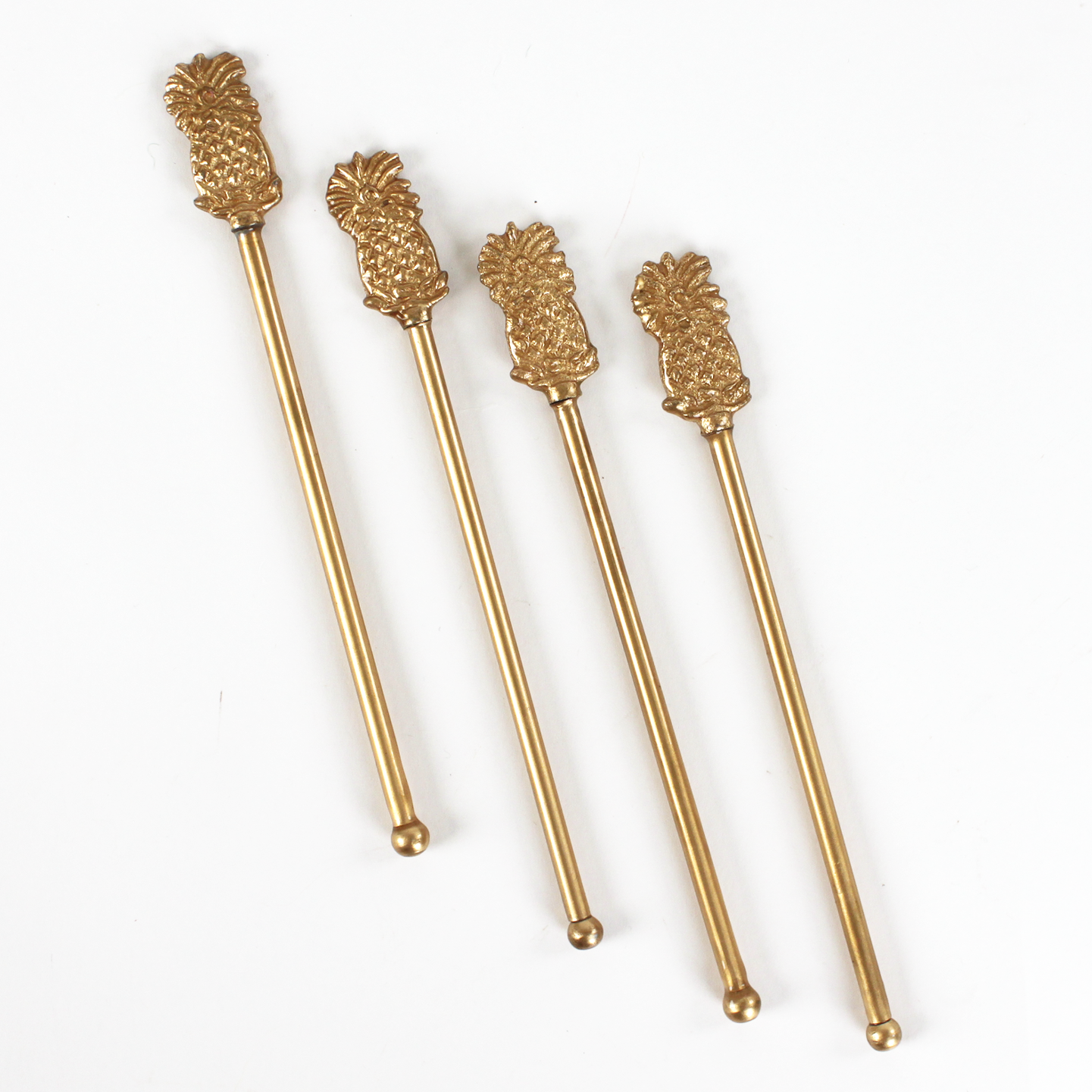 Four gold pineapple-shaped drink stirrers on a white background