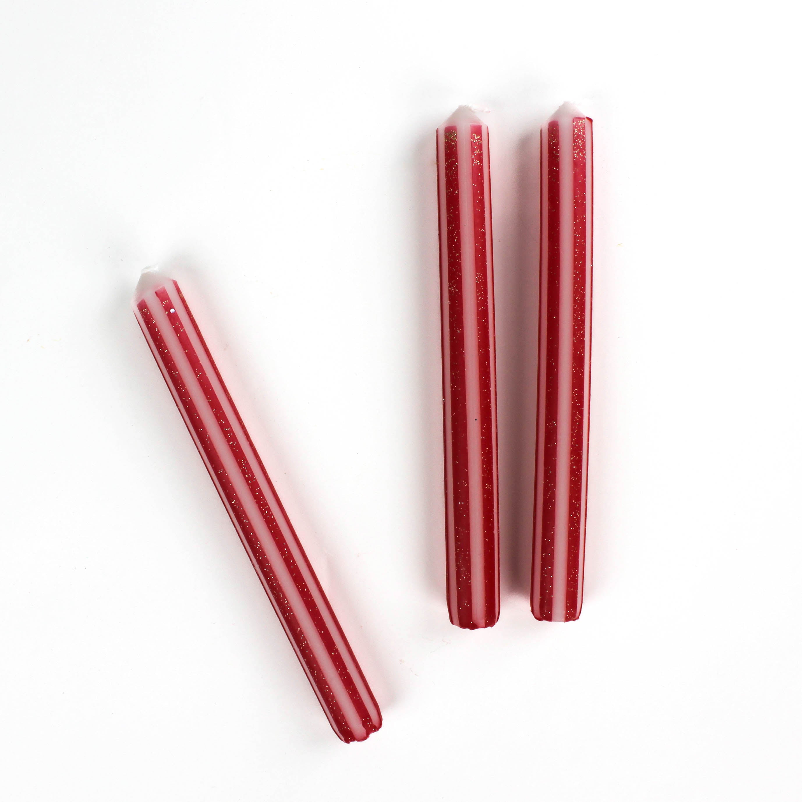 3 gold red and white striped taper candles lying in a white background