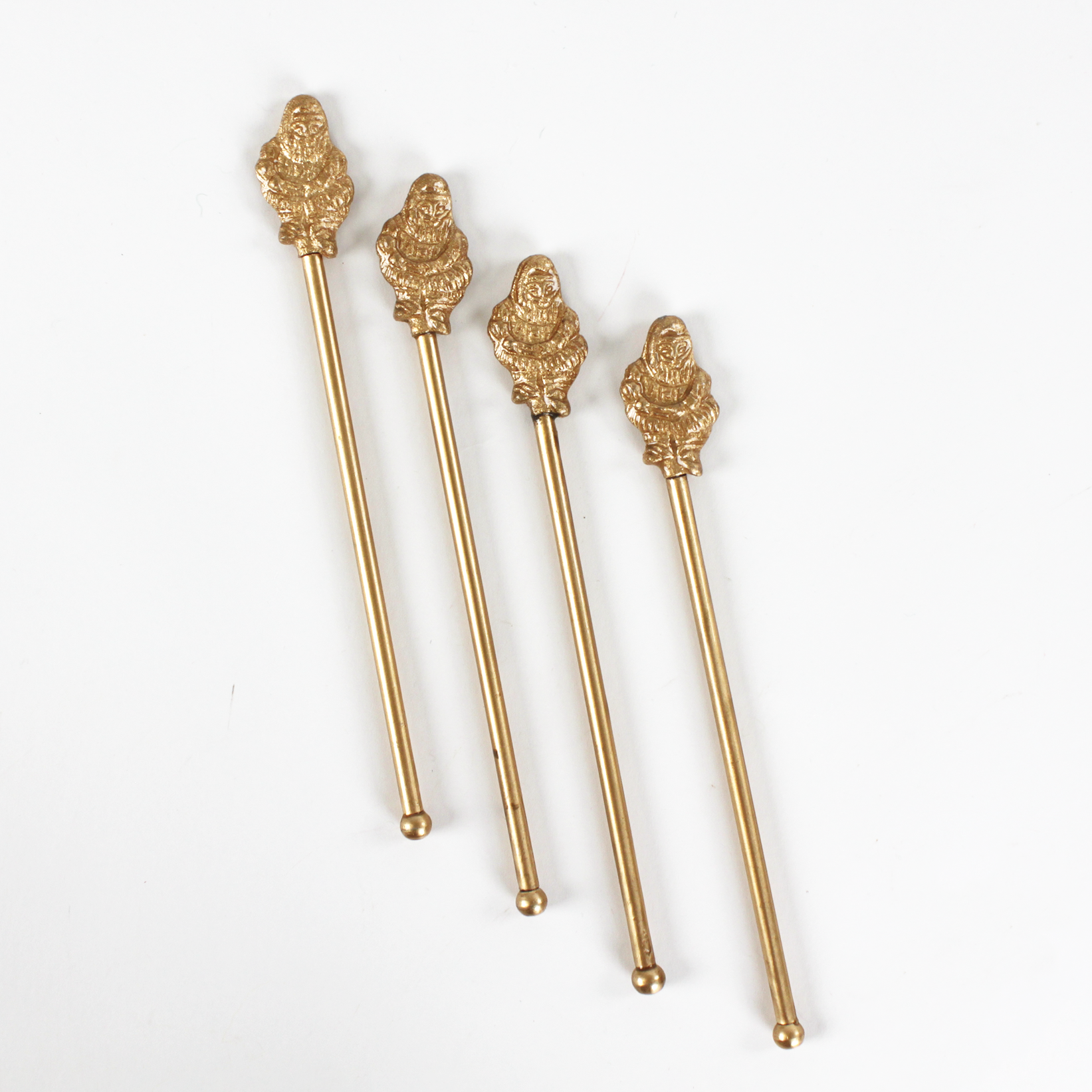Four gold christmas drinks stirrers with decorative santa ends on a white background