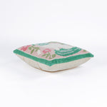 side view of a square decorative pillow with a hooked texture, featuring a white pug with green details surrounded by pink, white, and green floral accents on a blush pink background.