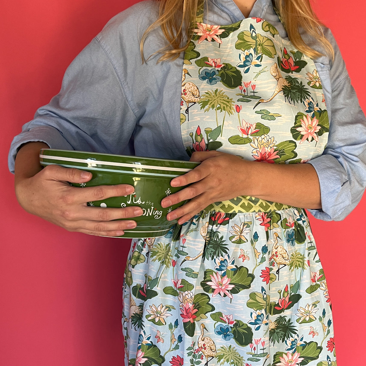 a woman wearing a green, pink and blue floral apron featuring the Meadow bluc water lilies pattern fabric from madcap cottage and holding a green bowl