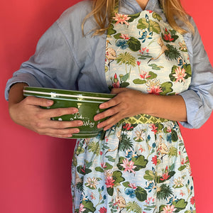 a woman wearing a green, pink and blue floral apron featuring the Meadow bluc water lilies pattern fabric from madcap cottage and holding a green bowl