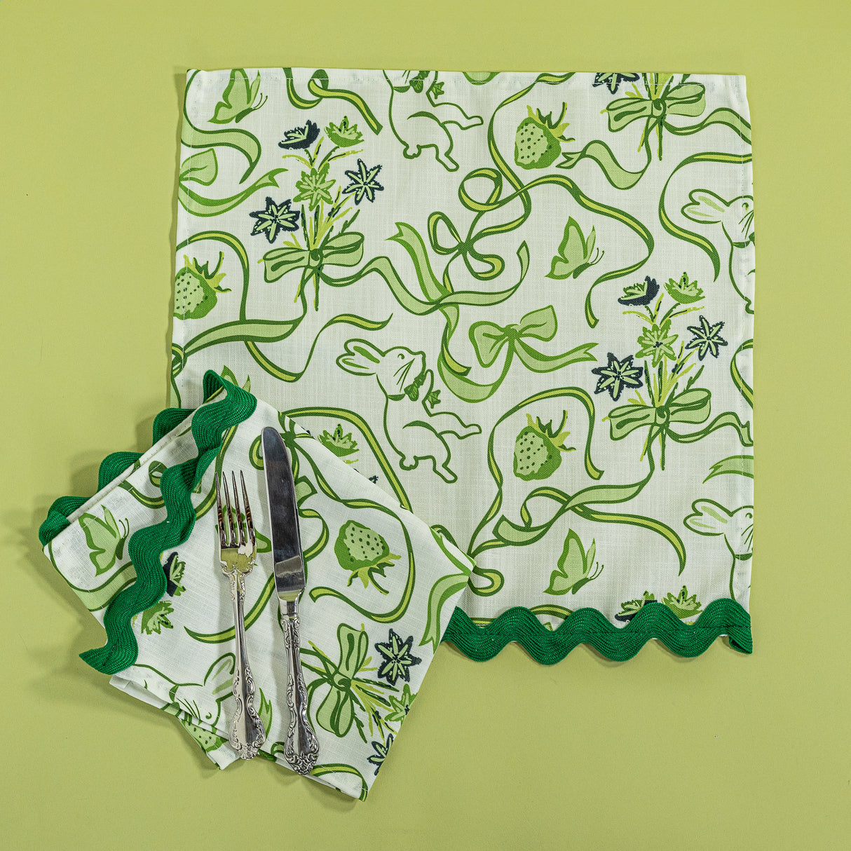 Bunnies and bow print clothnapkins in green with cutlery against a green background.