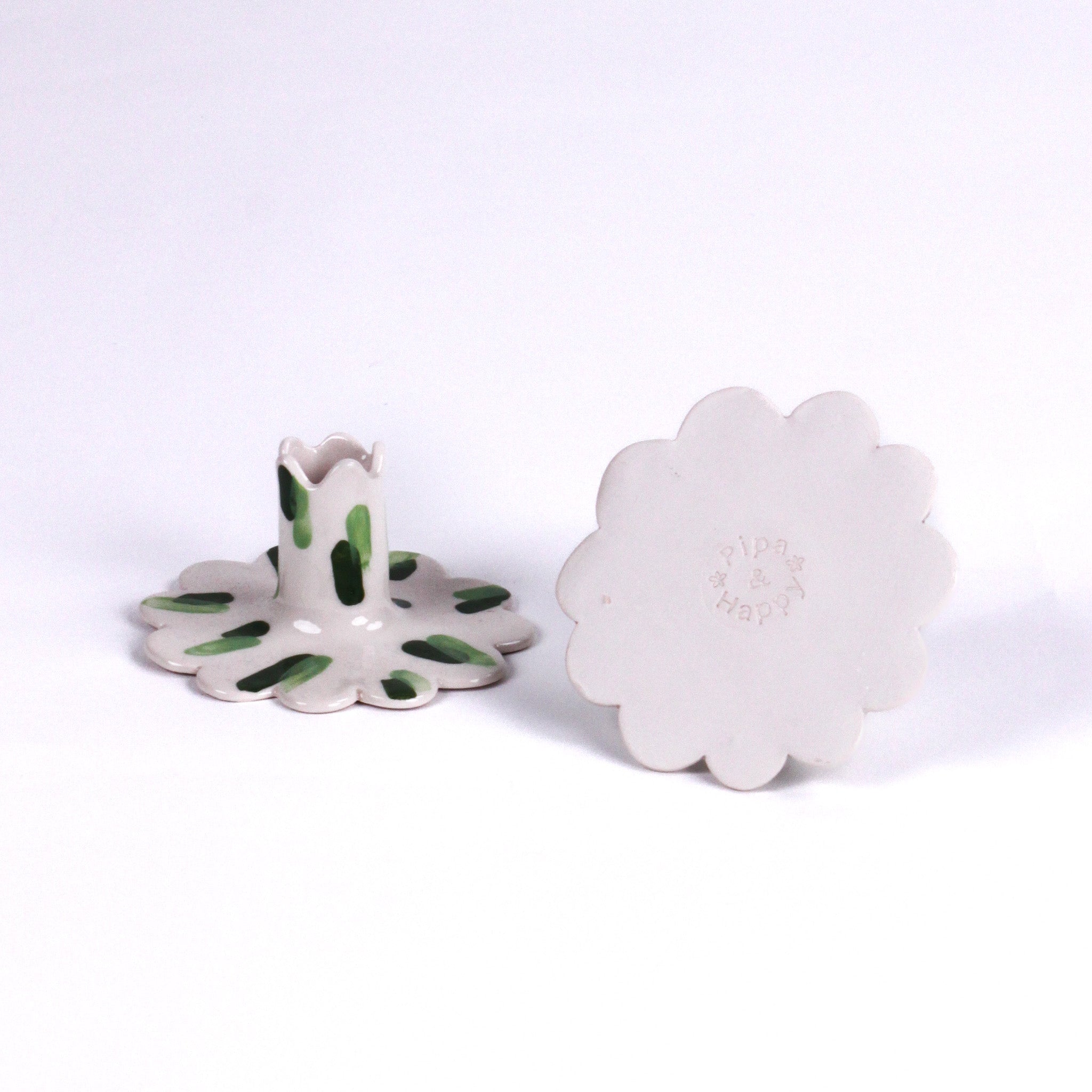 Set of two white ceramic scalloped taper candle holders with green brushstroke accents, shown from the top and side angles on a light background.