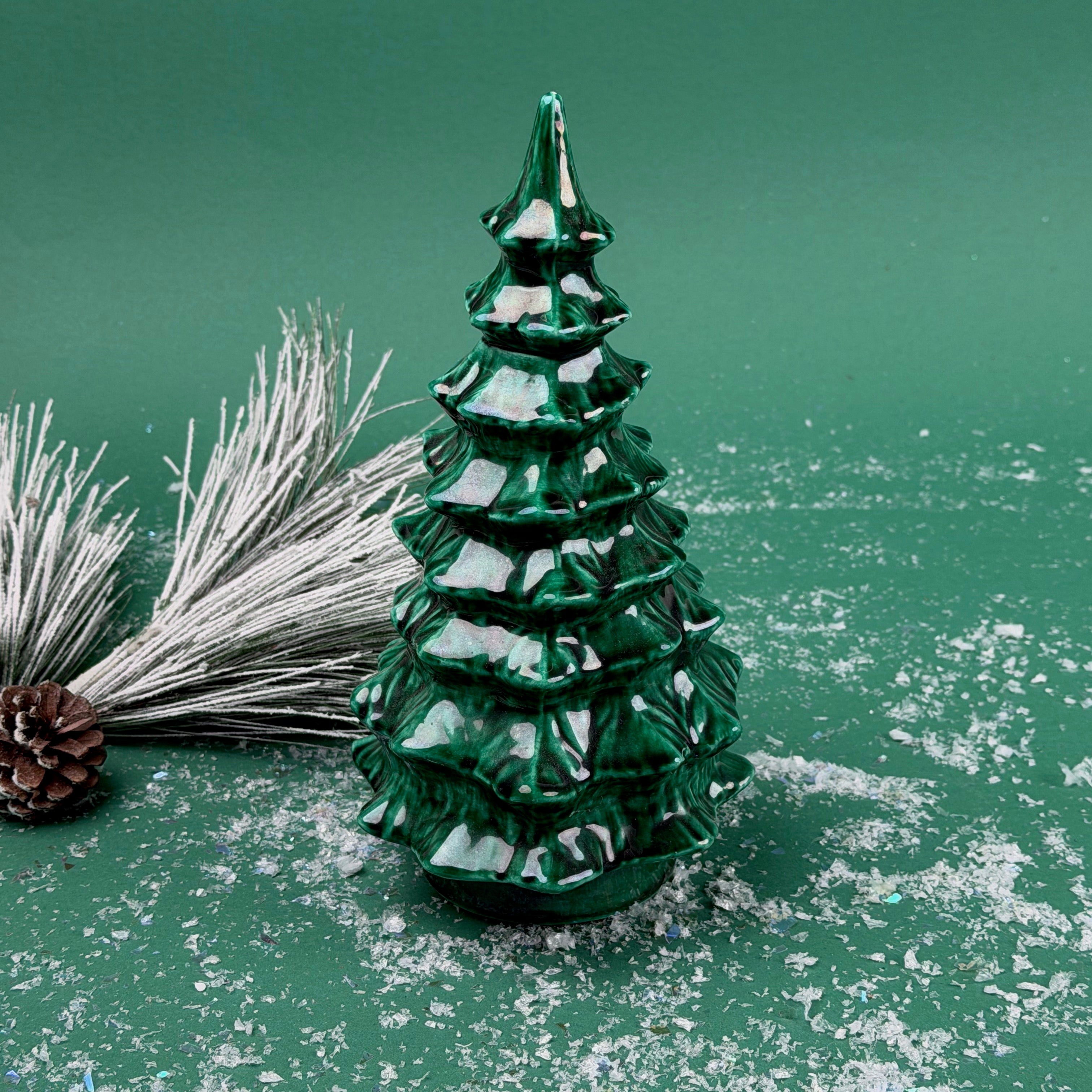 Green marbled ceramic Christmas tree decoration with frosted pine branches and pinecones on a snowy green background