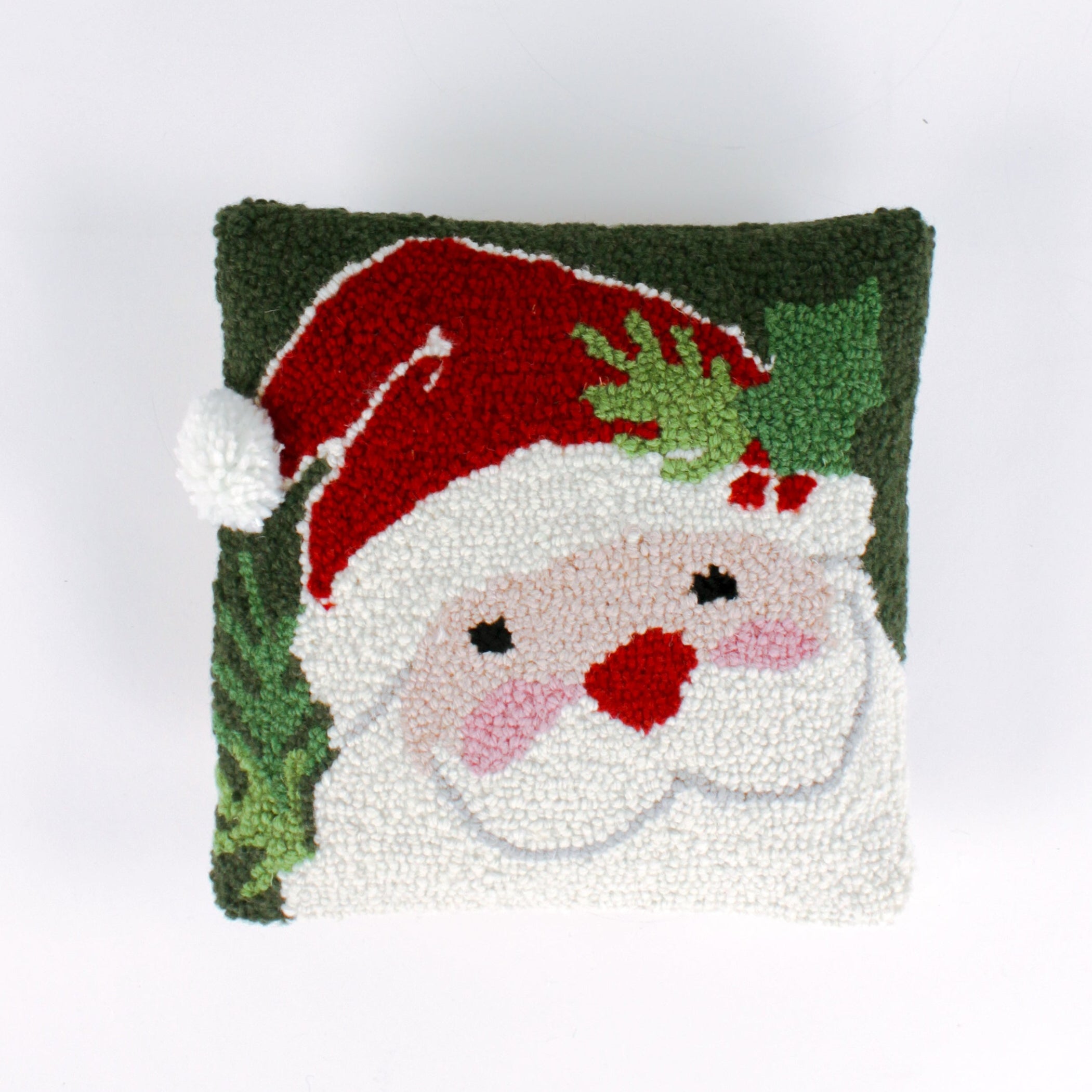 Square Christmas pillow featuring a hooked wool design of Santa Claus with rosy cheeks, a red hat, and green holly leaves on a dark green background.