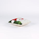 side of a Square Christmas pillow featuring a hooked wool design of Santa Claus with rosy cheeks, a red hat, and green holly leaves on a dark green background.