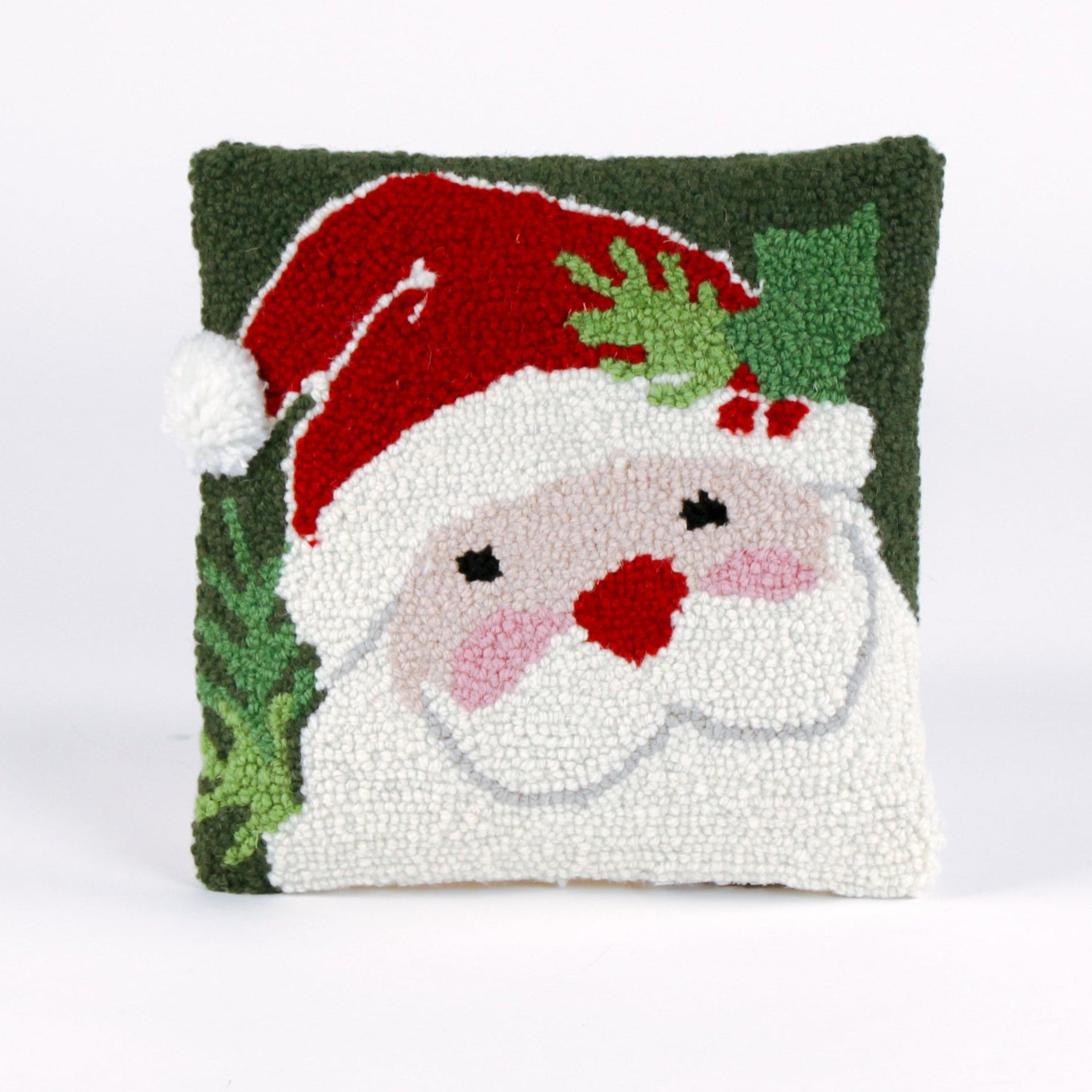 Square Christmas pillow featuring a hooked wool design of Santa Claus with rosy cheeks, a red hat, and green holly leaves on a dark green background.