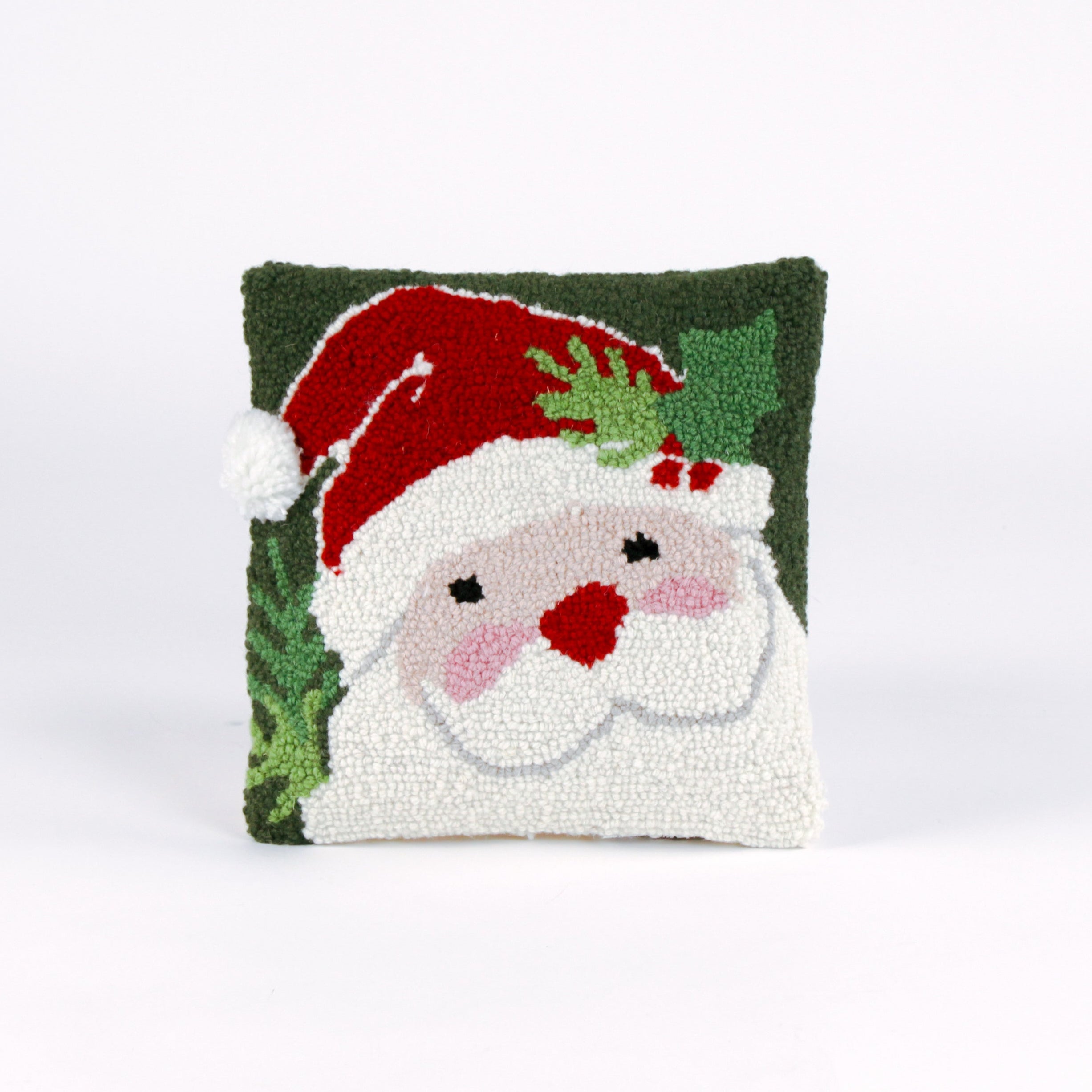 Square Christmas pillow featuring a hooked wool design of Santa Claus with rosy cheeks, a red hat, and green holly leaves on a dark green background.