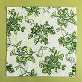 A green bunny and strawberry print fabric Easter napkin against a green background. 