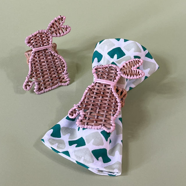 pair of rattan bunny napkin rings with one on a green dinner napkin