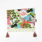 Folded Christmas tea towel featuring a colorful chinoiserie-inspired landscape print with green, pink, and blue tones, finished with a pink and green tassel accent.