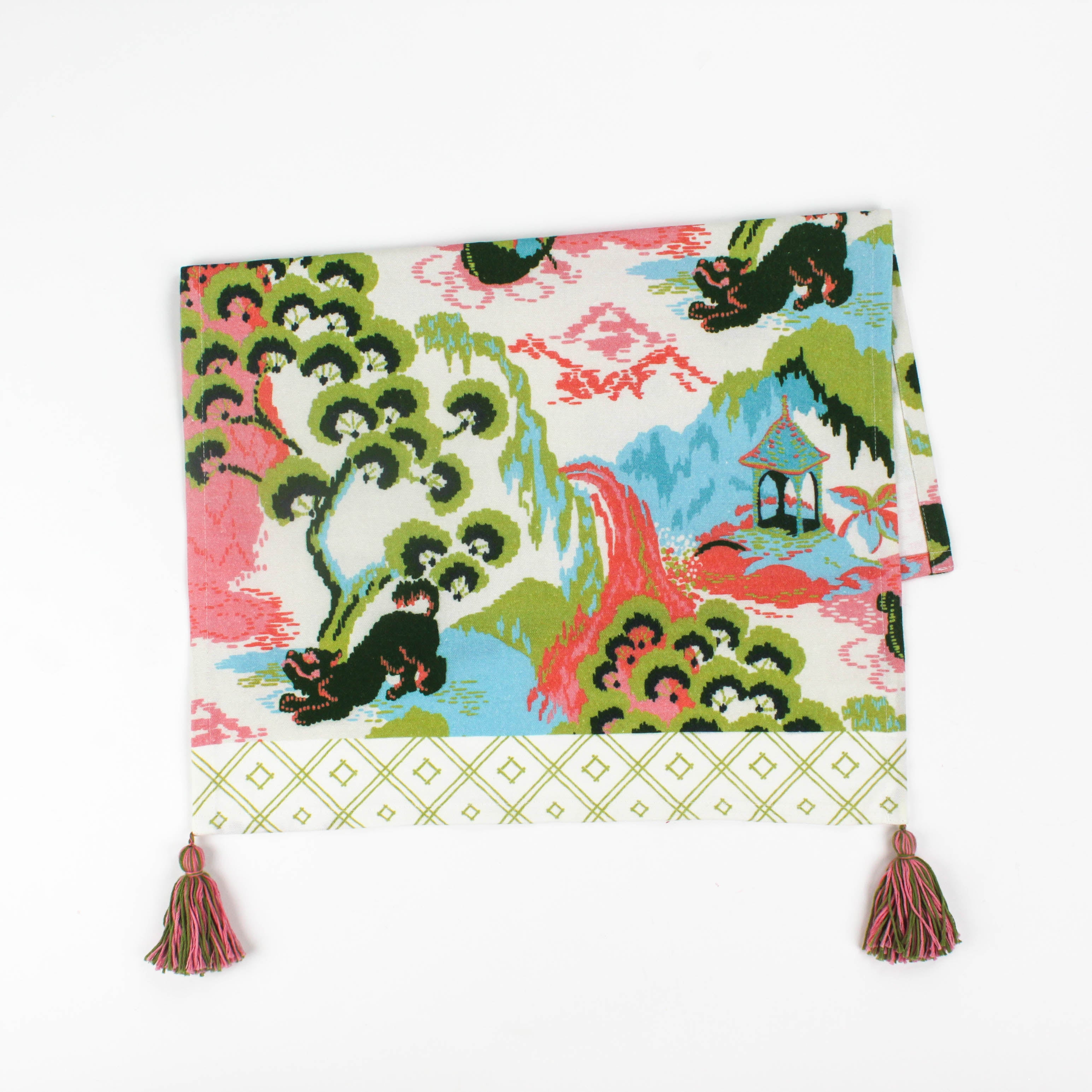 Folded Christmas tea towel featuring a colorful chinoiserie-inspired landscape print with green, pink, and blue tones, finished with a pink and green tassel accent.