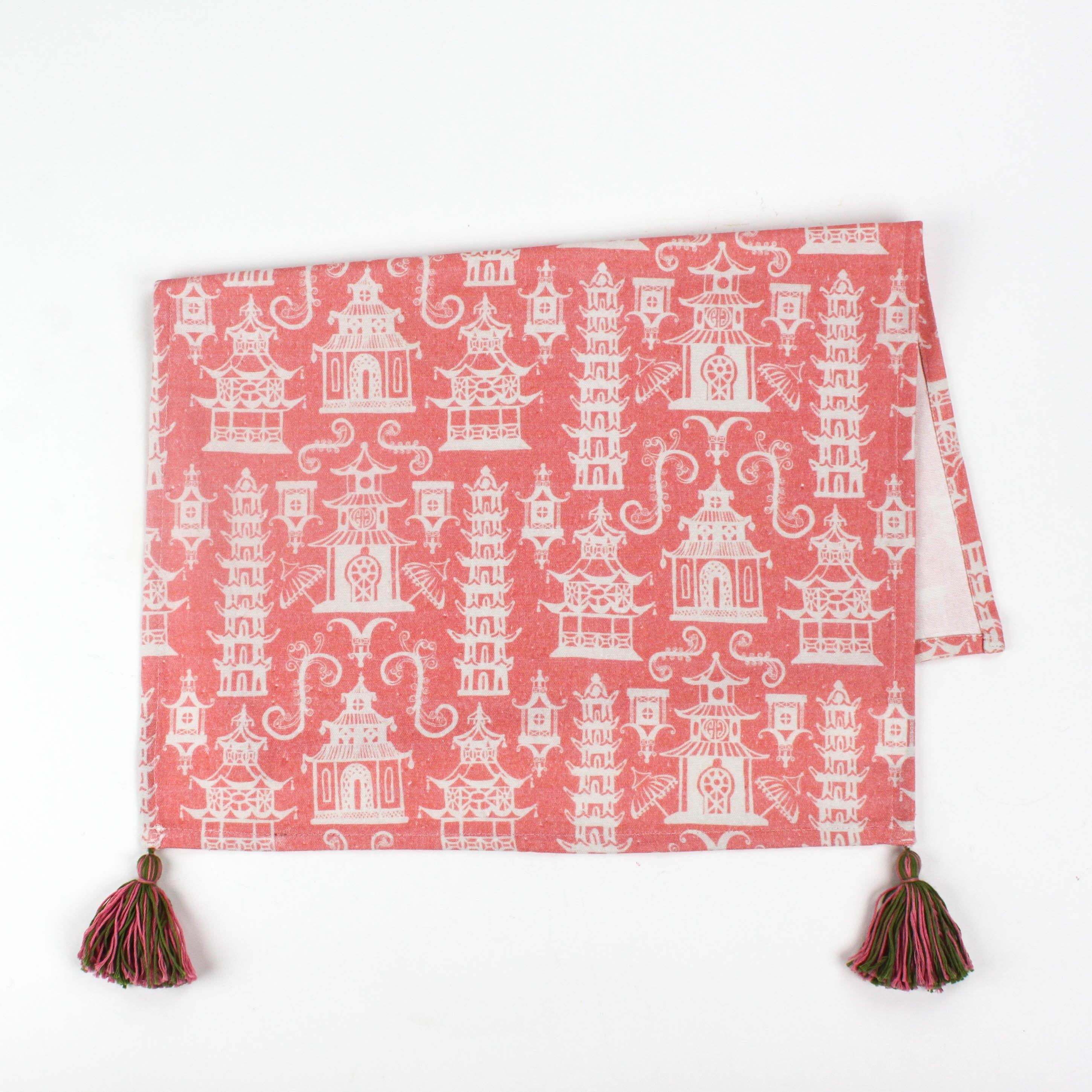 Half-folded Christmas tea towel with a pink and white chinoiserie pagoda pattern, featuring intricate architectural motifs and pink-green tassels on each corner.