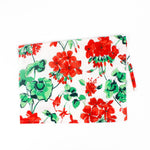 Folded Christmas tea towel featuring a festive red geranium floral print with green leaves on a white background, creating a bright holiday-inspired design.