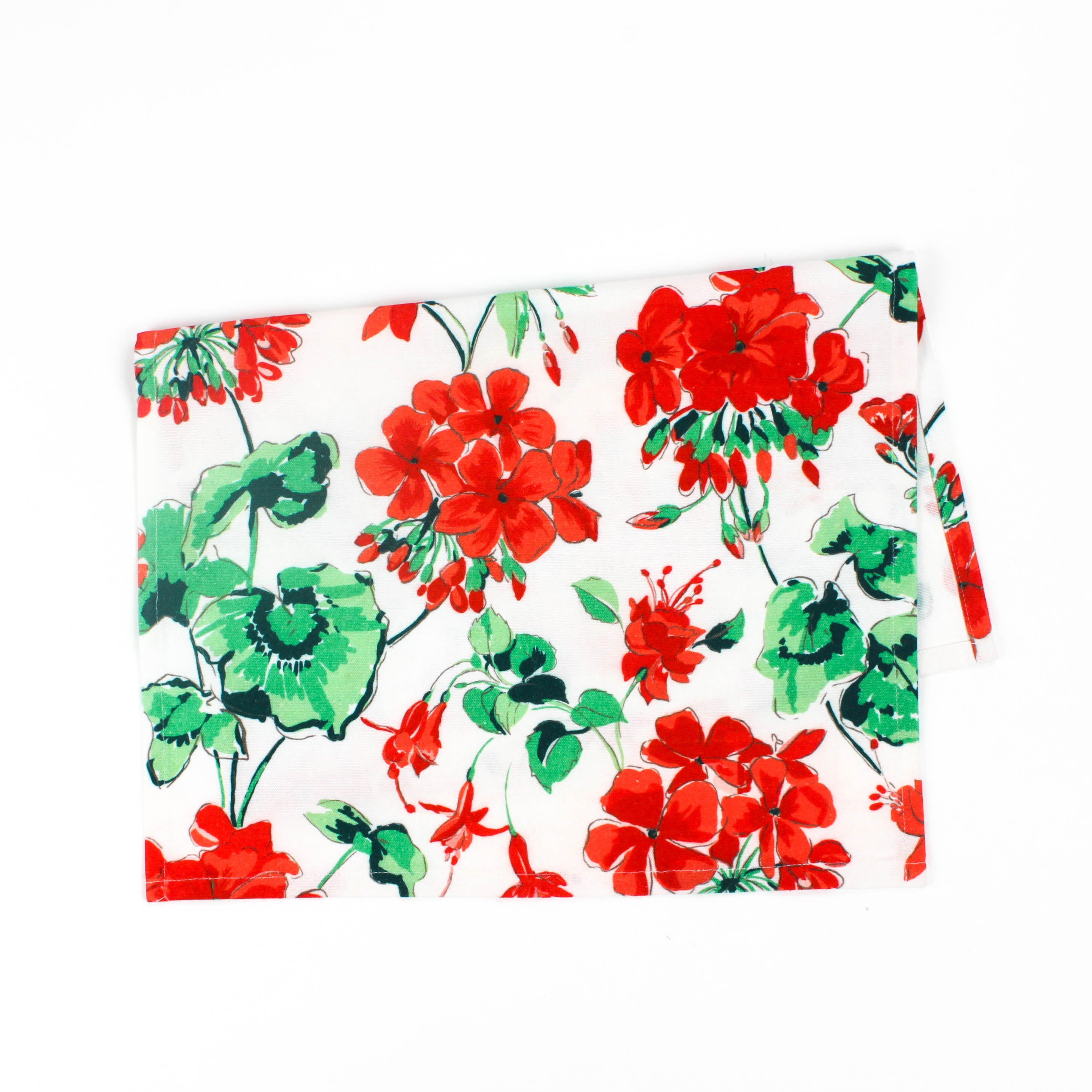 Folded Christmas tea towel featuring a festive red geranium floral print with green leaves on a white background, creating a bright holiday-inspired design.