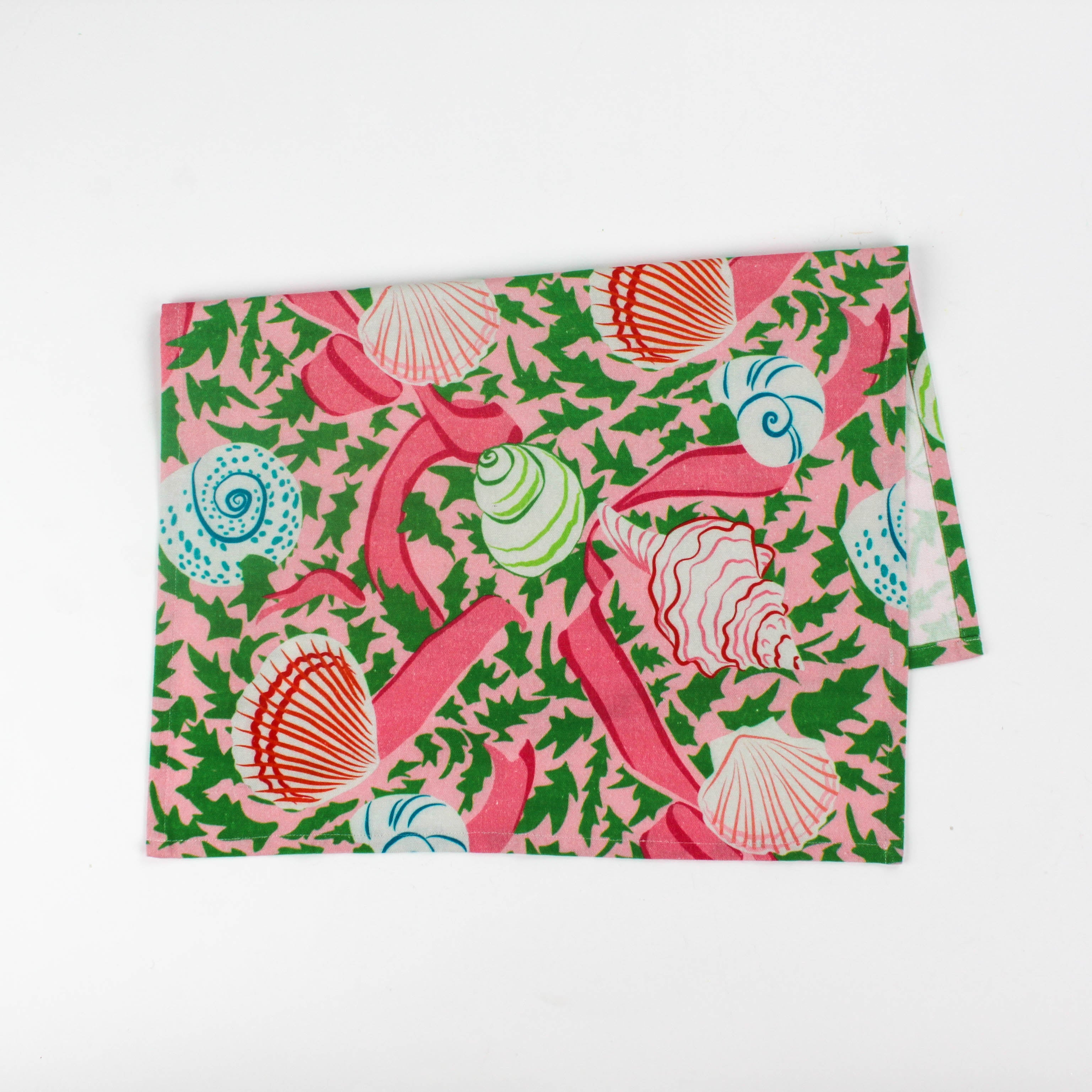 Folded Christmas tea towel featuring a pink background with colorful seashell and ribbon patterns accented by green holly-like leaves for a festive coastal look.