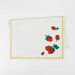 Folded Christmas tea towel with a white background, decorated with strawberries and green leaves in one corner, bordered by a thin yellow trim.