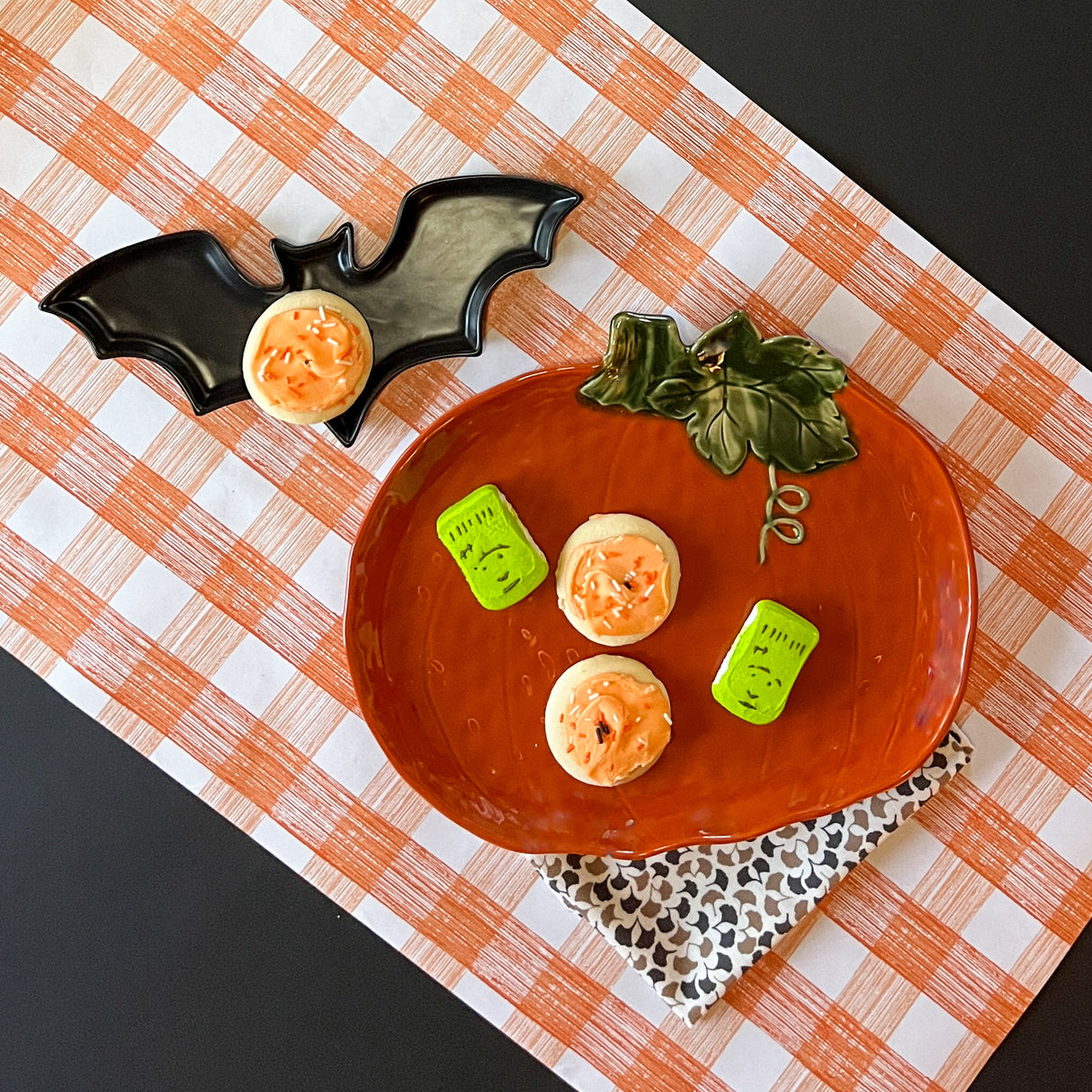 a large orange pumpkin serving platter with 5 halloween cookies on it against an orange paper halloween table runner. 