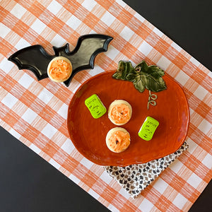 a large orange pumpkin serving platter with 5 halloween cookies on it against an orange paper halloween table runner. 