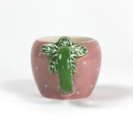 a pink ceramic strawberry mug with a green leafy handle