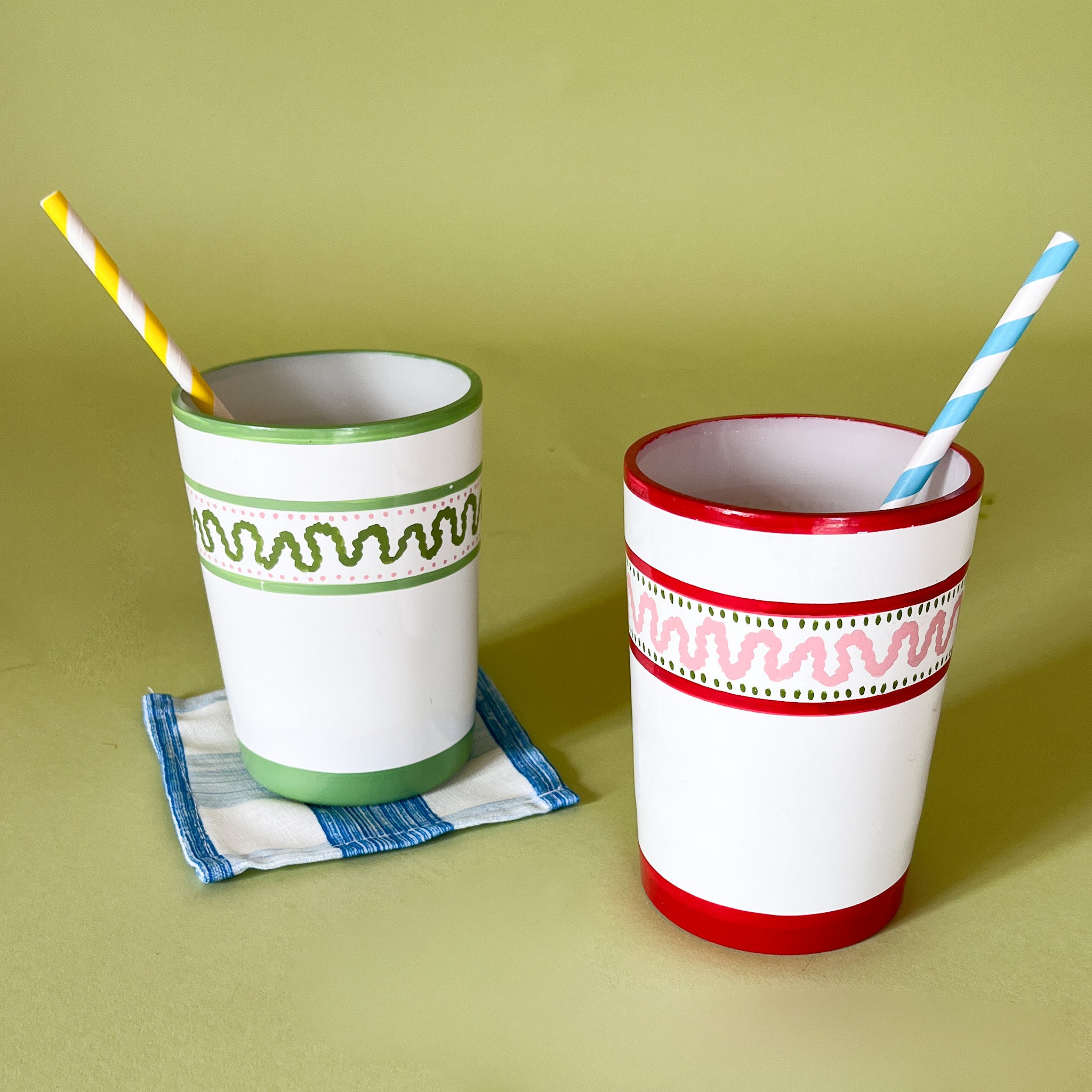 Two hand-painted glasses with striped patterns, one with a green top and the other with a red top, both with straws.