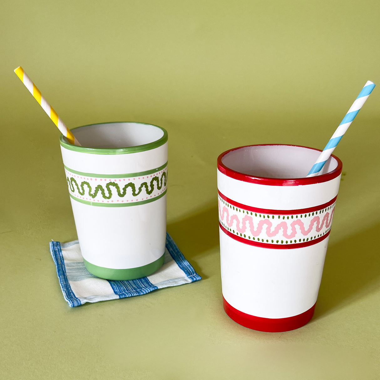 Two hand-painted glasses with striped patterns, one with a green top and the other with a red top, both with straws.