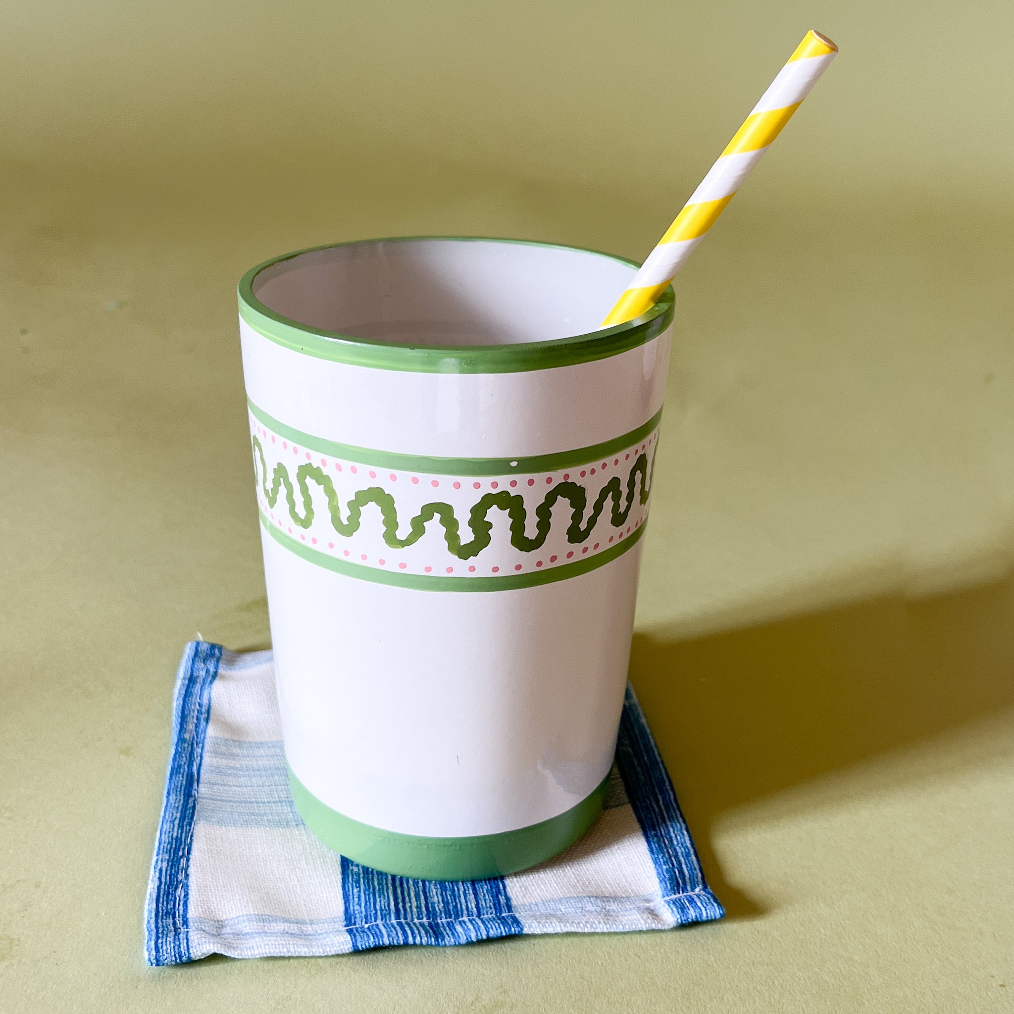 a hand-painted glass with green striped pattern, with a green top and with straw