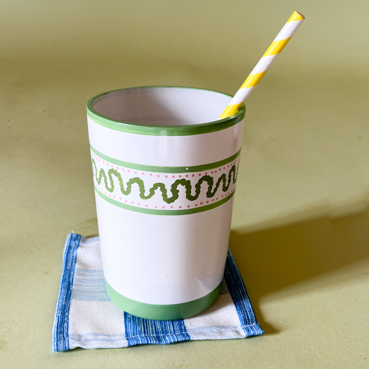 a hand-painted glass with green striped pattern, with a green top and with straw