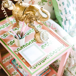 A pink side table with green and white striped accents and an elephant phone and notepad resting on top. 