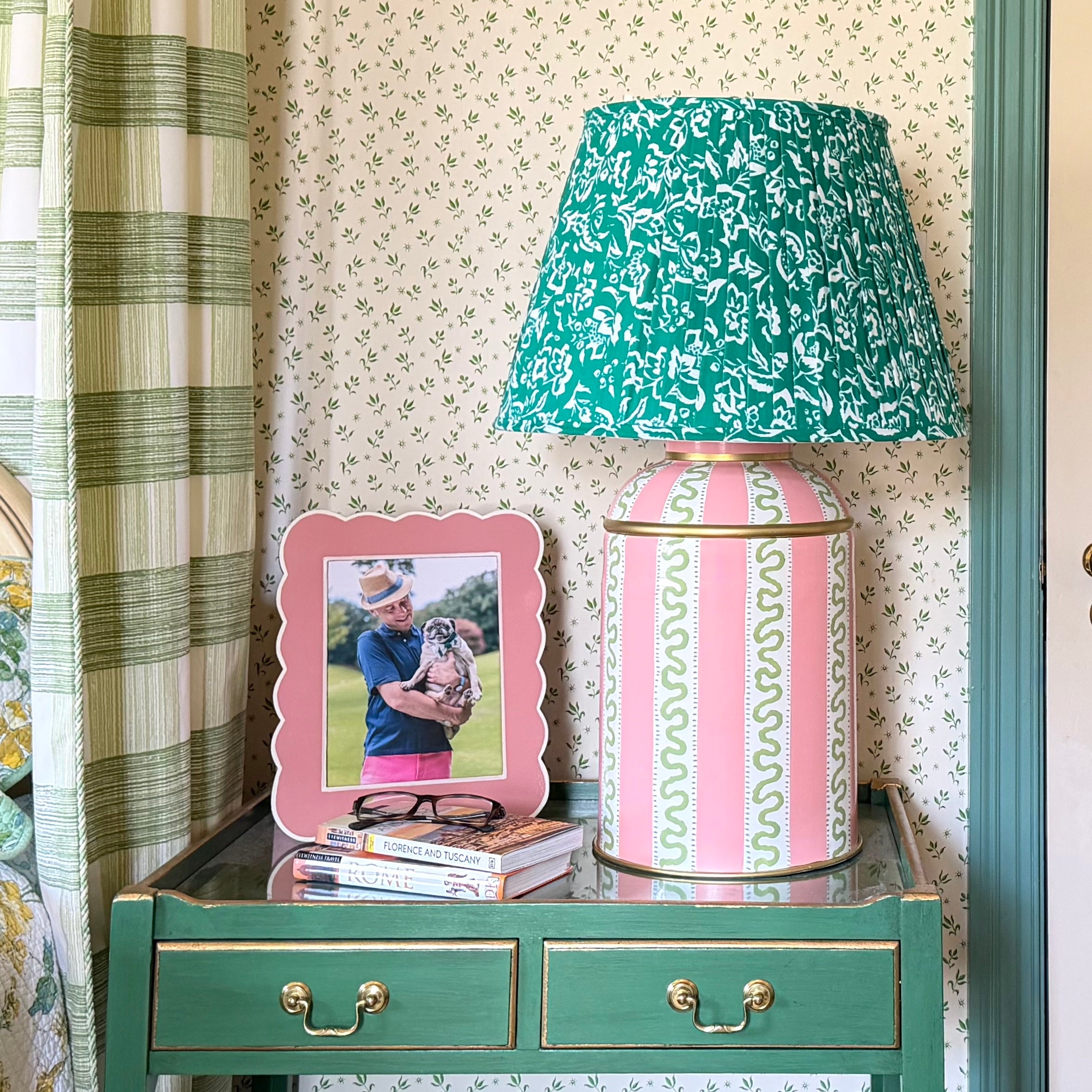 Decorative pink striped lamp with a patterned shade on a nightstand next to a framed photo and books.