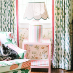 a striped white, pink and green lamp with a scalloped rattan shade with green trim sitting on a pink side table all from madcap cottage
