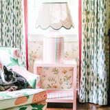 a striped white, pink and green lamp with a scalloped rattan shade with green trim sitting on a pink side table all from madcap cottage