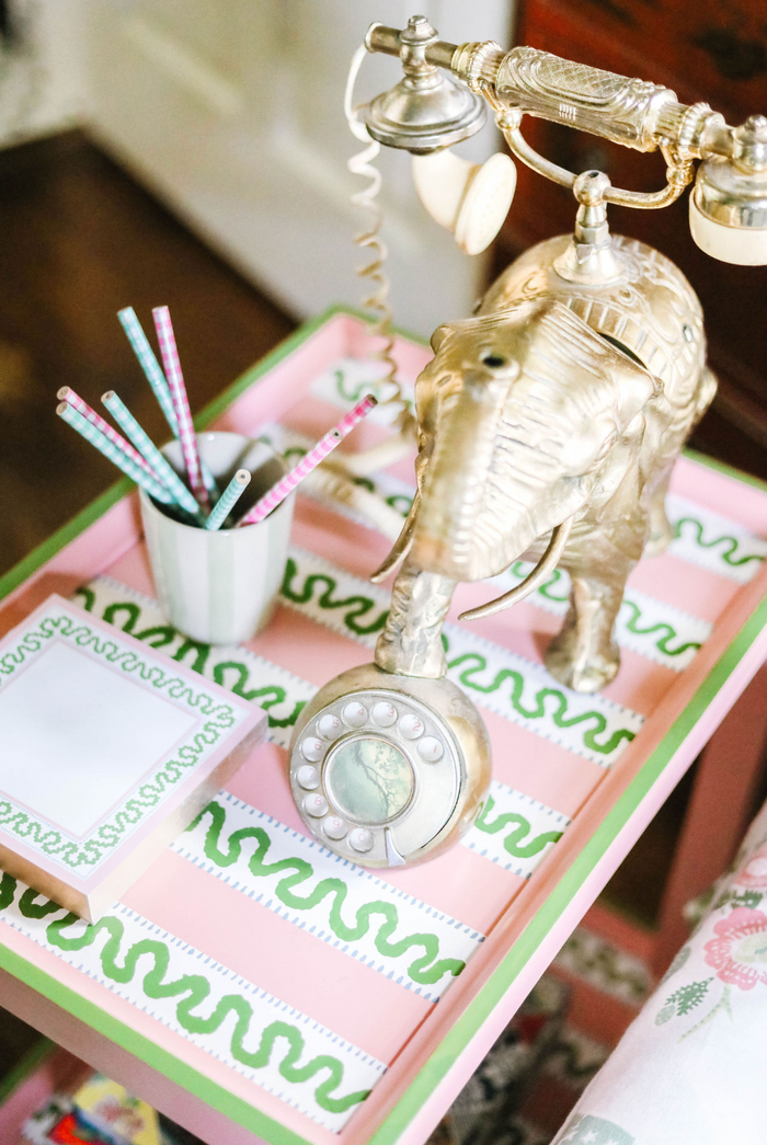 A pink side table with green and white striped accents and an elephant phone and notepad resting on top. 