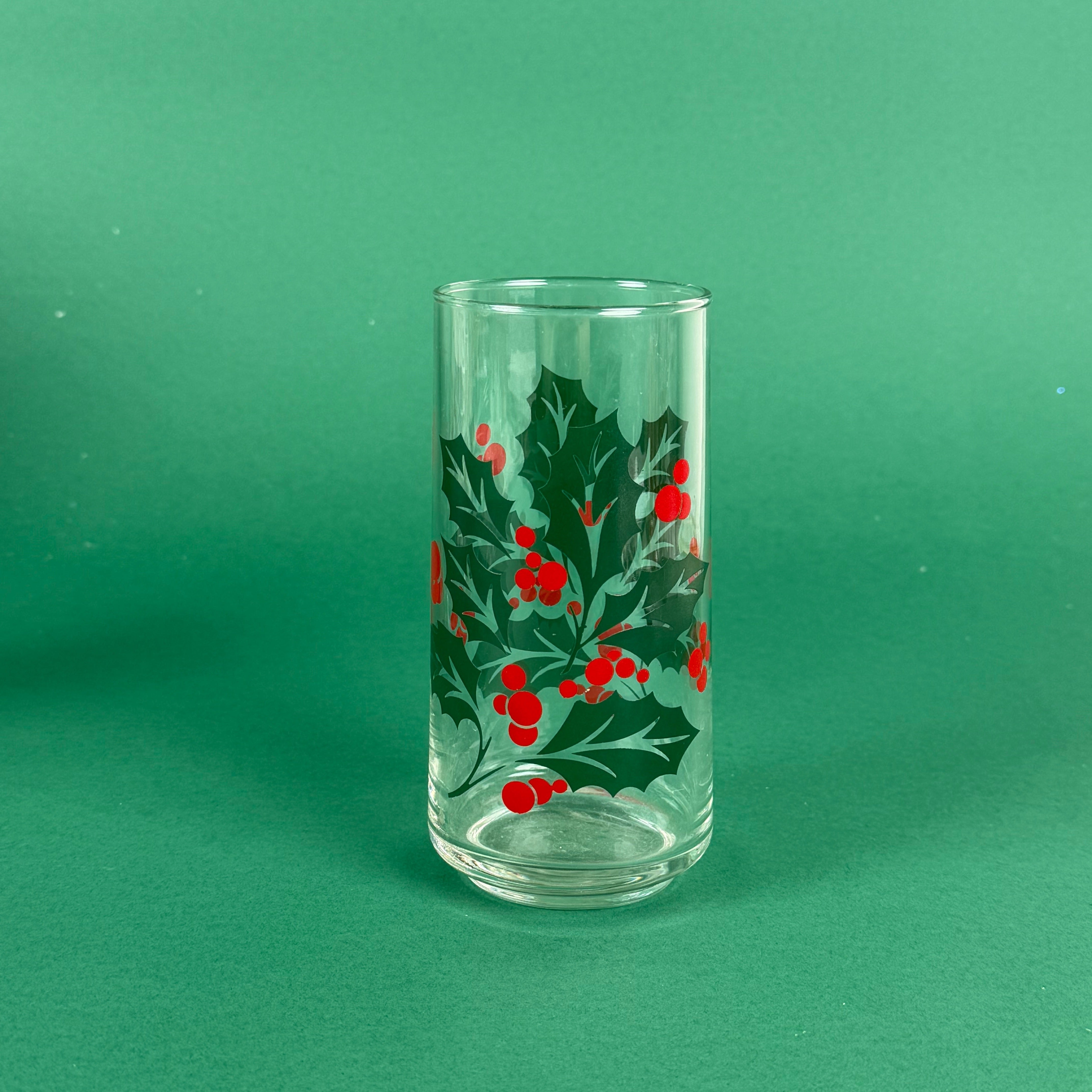 Clear highball glass with green holly leaves and red berry design on a green background