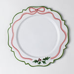 A white tole metal christmas charger with a pink ribbon and holly motifs around the edges against a white background.  