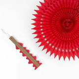 A folded red honeycomb paper fan decoration with an attached wooden support strip beside an opened fan on a white background.