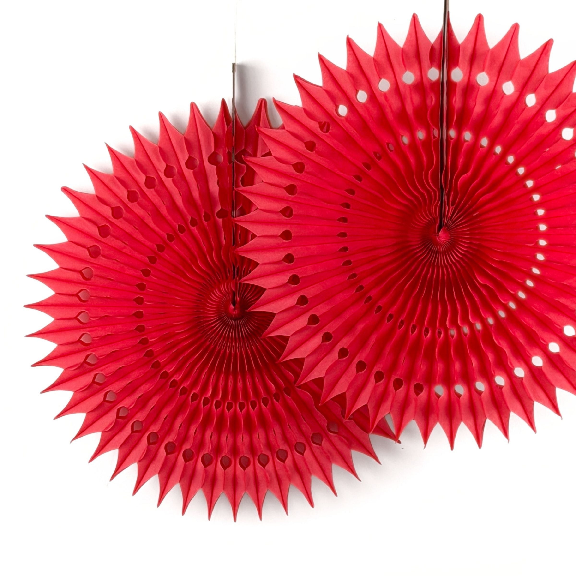 A red honeycomb paper fan decoration with a starburst design hanging against a white background.
