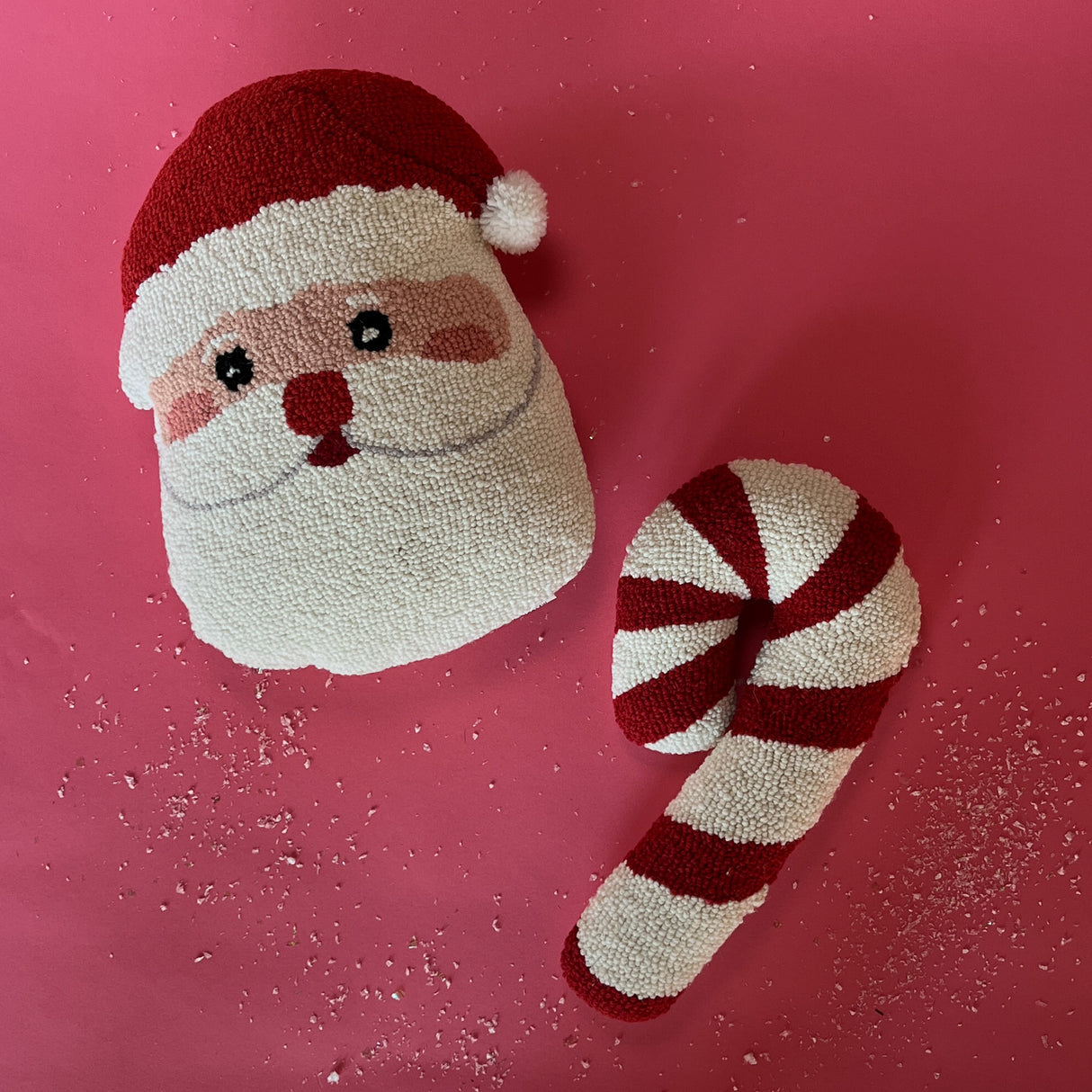 two hooked wool christmas pillows on a red background one in the shape of a candy cane, the other a jolly santa face