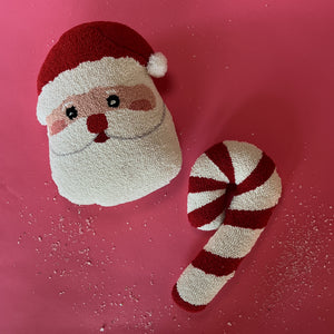 two hooked wool christmas pillows on a red background one in the shape of a candy cane, the other a jolly santa face