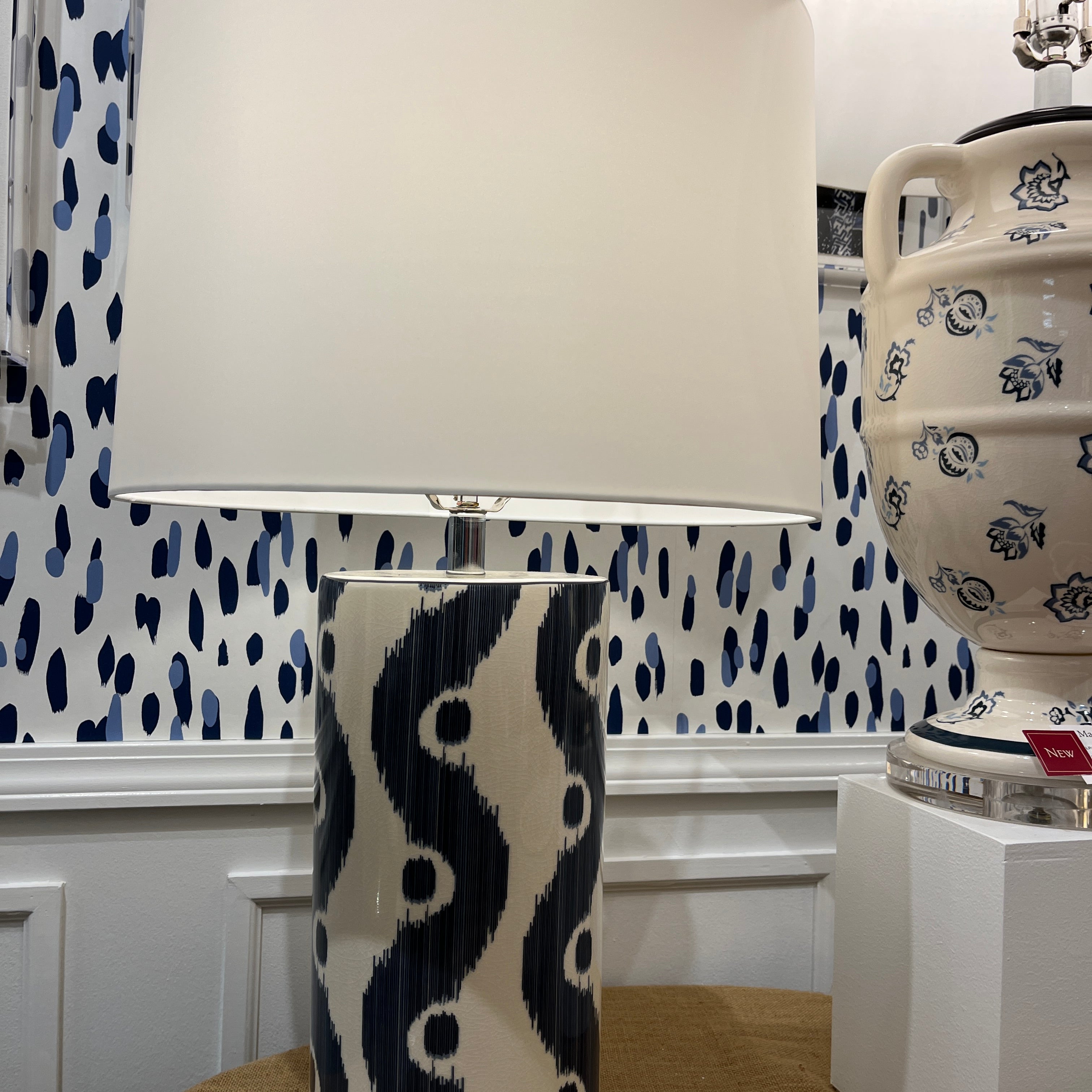 An illuminated blue and white table lamp featuring a white porcelain base with blue squiggle motif and a white lampshade.