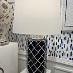 An illuminated navy blue and white table lamp with a navy blue porcelain base featuring a white lattice pattern and a plain white lampshade.
