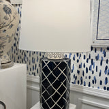 An illuminated navy blue and white table lamp with a navy blue porcelain base featuring a white lattice pattern and a plain white lampshade.