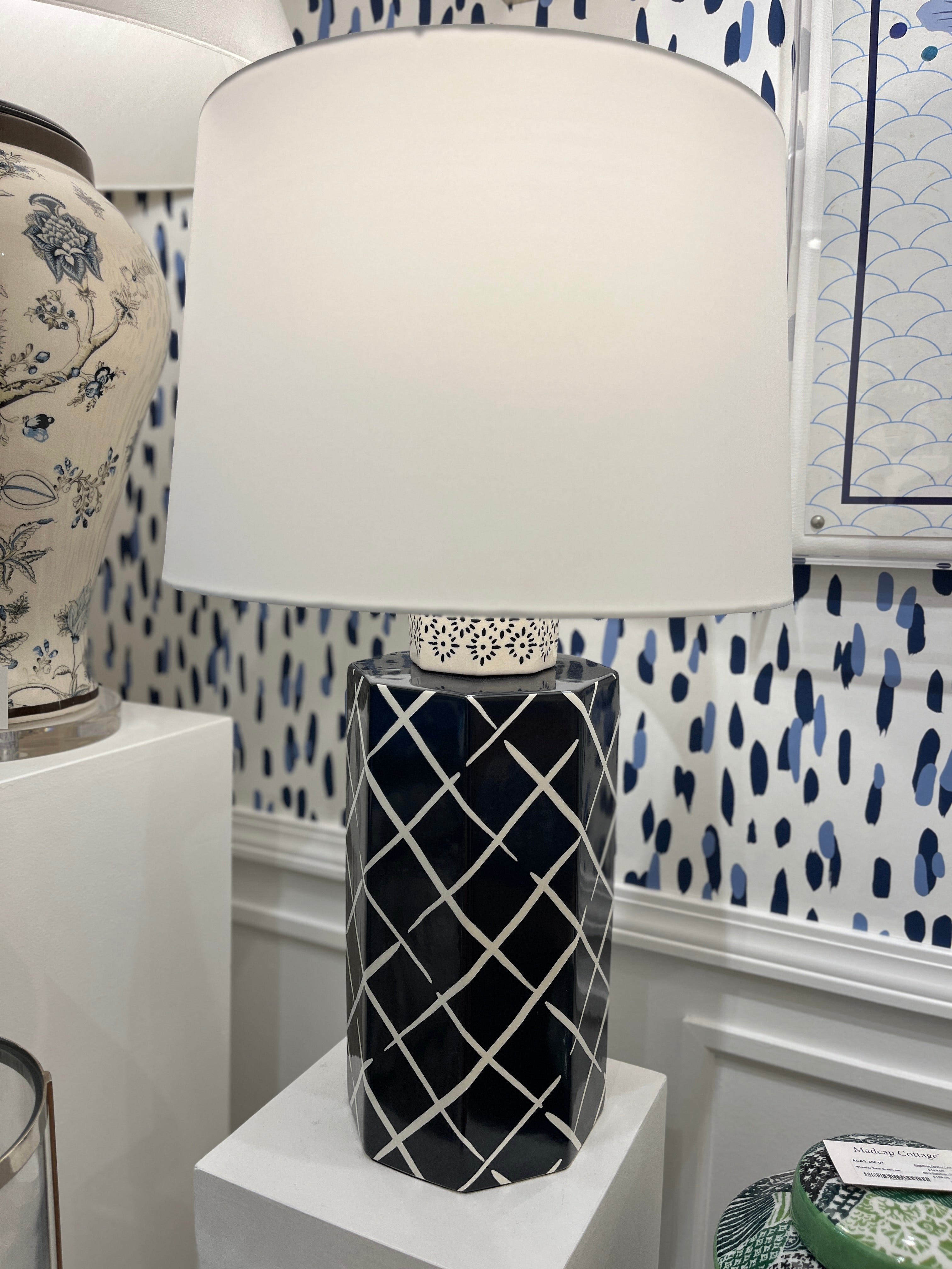 An illuminated navy blue and white table lamp with a navy blue porcelain base featuring a white lattice pattern and a plain white lampshade.