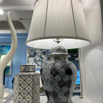 An illuminated navy table lamp with a navy blue patterned base and white shade.